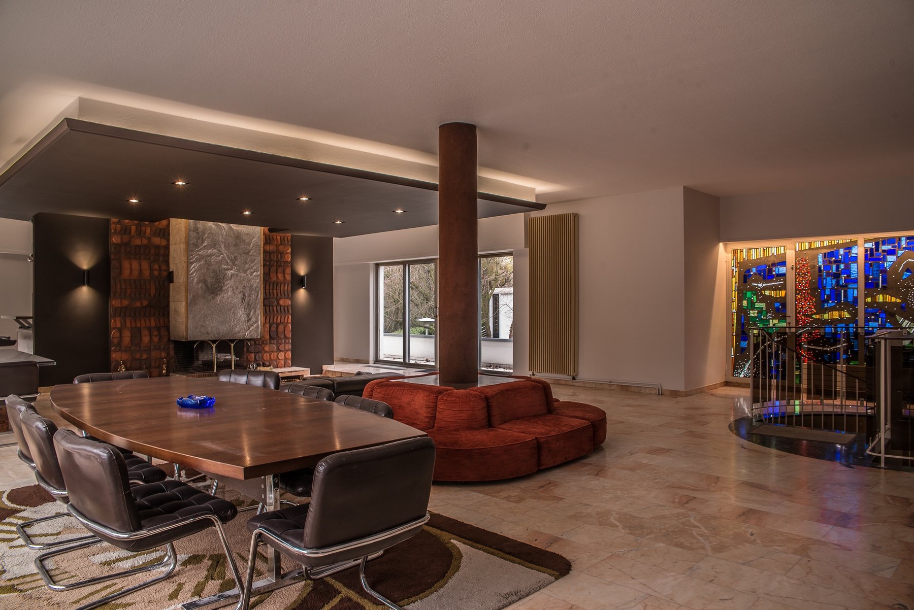 La Villa 70's — salon rétro avec table bois, canapé rouge et vitraux colorés